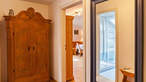 Un armari de fusta, una porta que dona a una habitació amb un llit i una cadira, i un mirall gran.