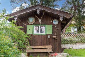Une cabane en bois rustique avec une fenêtre verte, un banc à l’extérieur et des bois de cerf accrochés au mur.