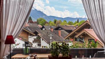 Blick durch ein Fenster mit Vorhängen, zeigt einen Berg und Wohnhäuser.