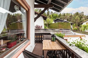Uma varanda com mesa e cadeiras de madeira, um candeeiro decorativo e vista para uma encosta arborizada.