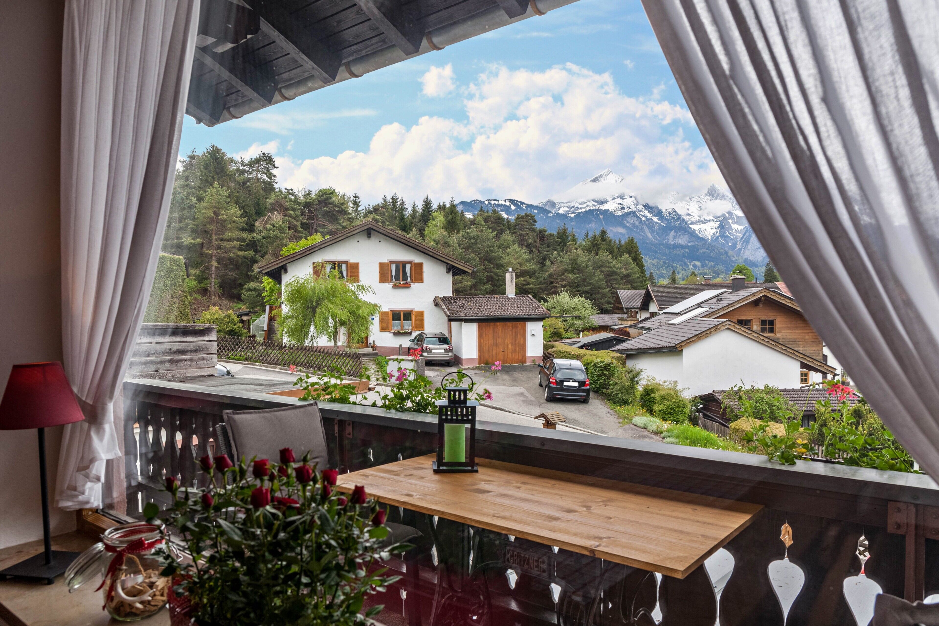 Ein Balkon mit Blick auf einen Berg, ein Holztisch, eine rote Lampe und ein Glas mit Blumen.