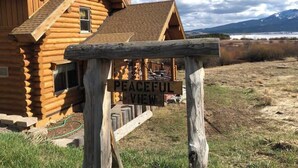 Une cabane en rondins sur laquelle est accroché un panneau indiquant « Vue paisible », entourée d’un champ verdoyant et avec des montagnes en arrière-plan.