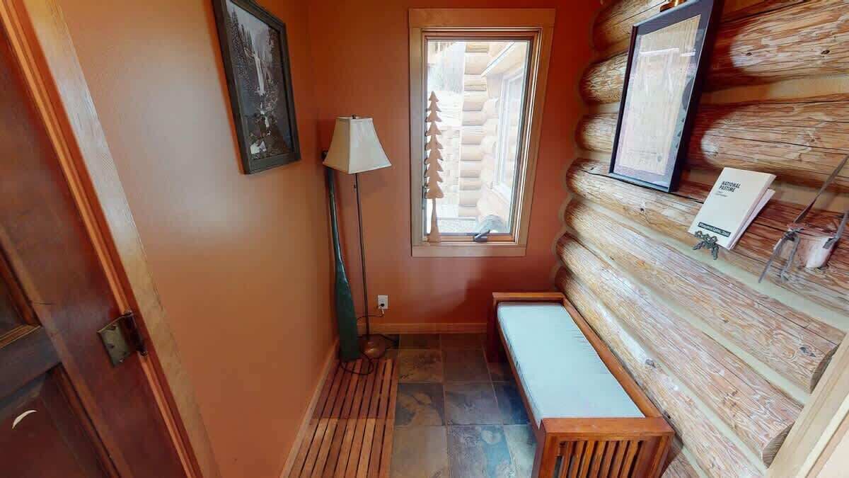 Interior de cabana de madeira com um banco, um abajur, um quadro e uma janela com silhueta de árvore.