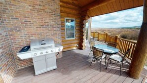 Un espace extérieur abrité comprenant un barbecue, une table avec des chaises et une vue sur le paysage.
