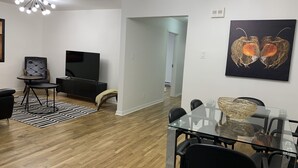 Una sala de estar moderna con televisor, asientos y un comedor con mesa de vidrio.