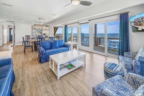 A spacious living room with a large sofa, a coffee table, and a view of the ocean through large sliding doors. - Soundfront Home w/ Hot Tub, Private Launch Dock, Windsports Access. Winds Up! (Avon)