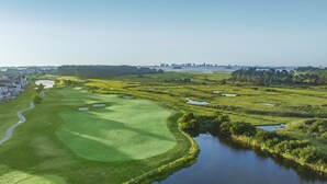 Un parcours de golf avec des obstacles d’eau, un étang et une zone résidentielle en arrière-plan.