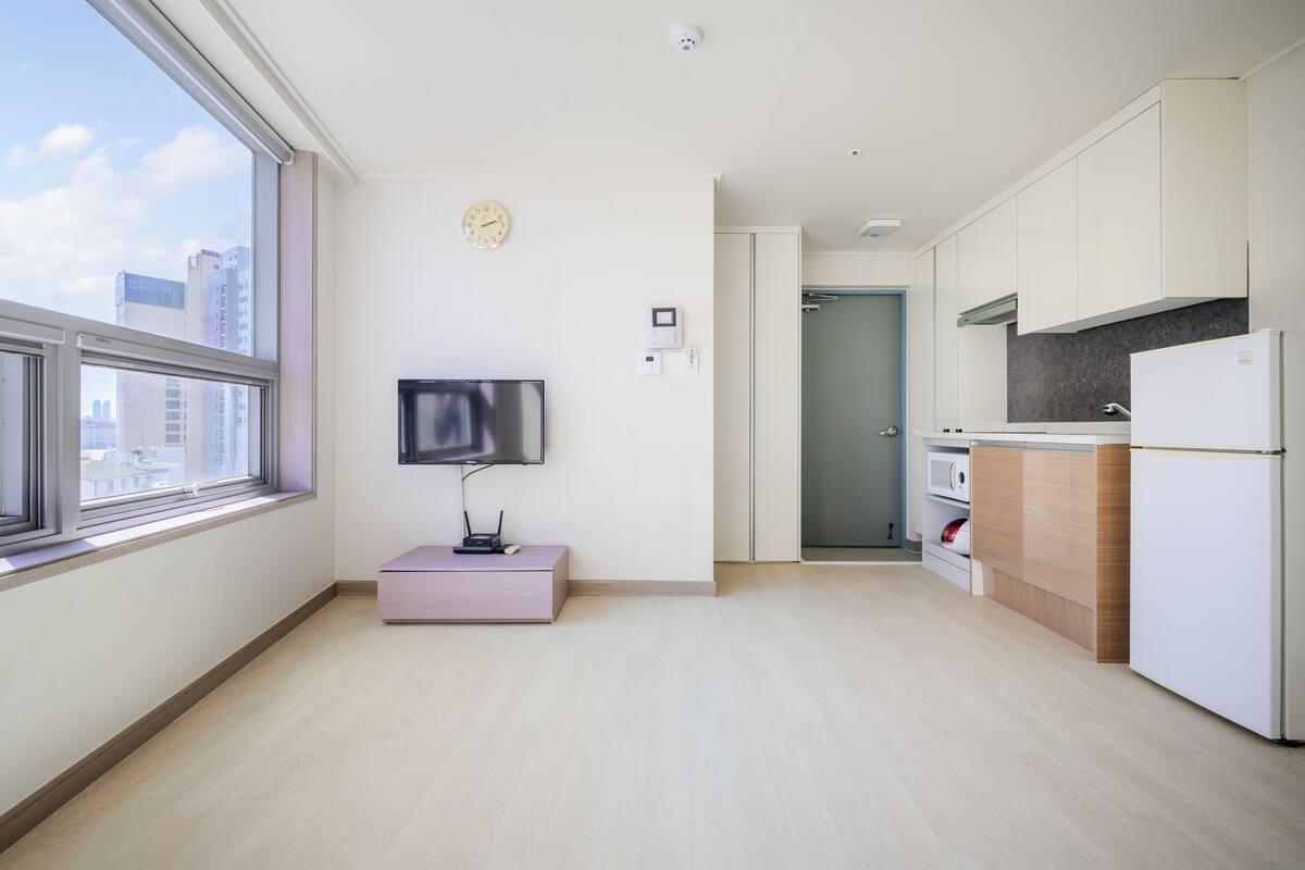 Un appartement moderne doté d’une cuisine, d’un téléviseur et d’une fenêtre offrant une vue sur les immebles.