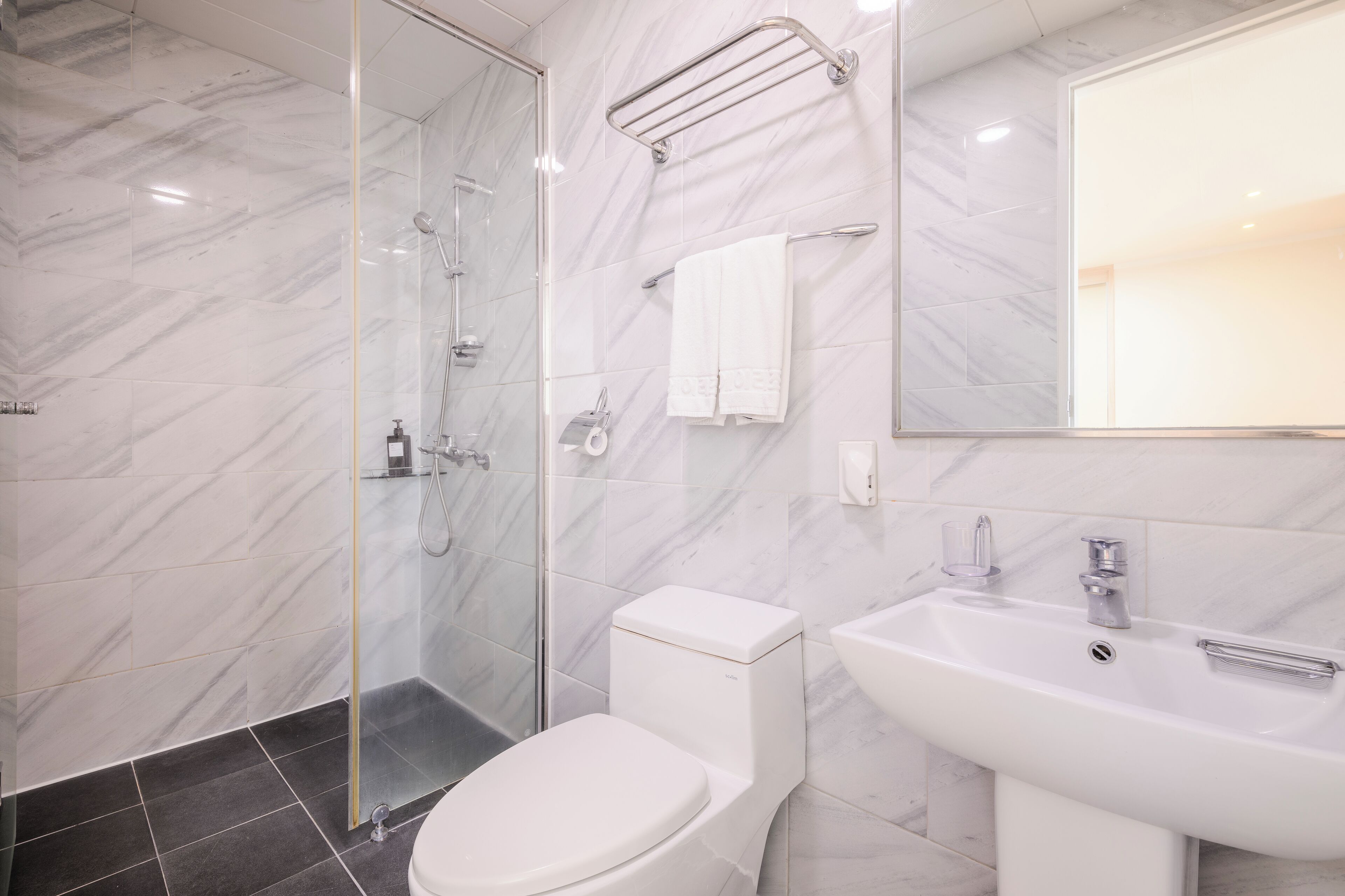 A modern bathroom with a glass shower enclosure, a white toilet, a sink with a mirror, and marble walls.