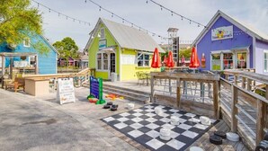 Un paseo marítimo con mesas al aire libre, una mesa de juego a cuadros y edificios coloridos.