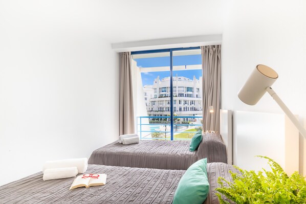 Habitación de hotel con cama, ventana con cortinas, lámpara y vista a un edificio.