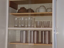 Un mueble de cocina con repisas que contienen diferentes objetos de vidrio y recipientes metálicos.