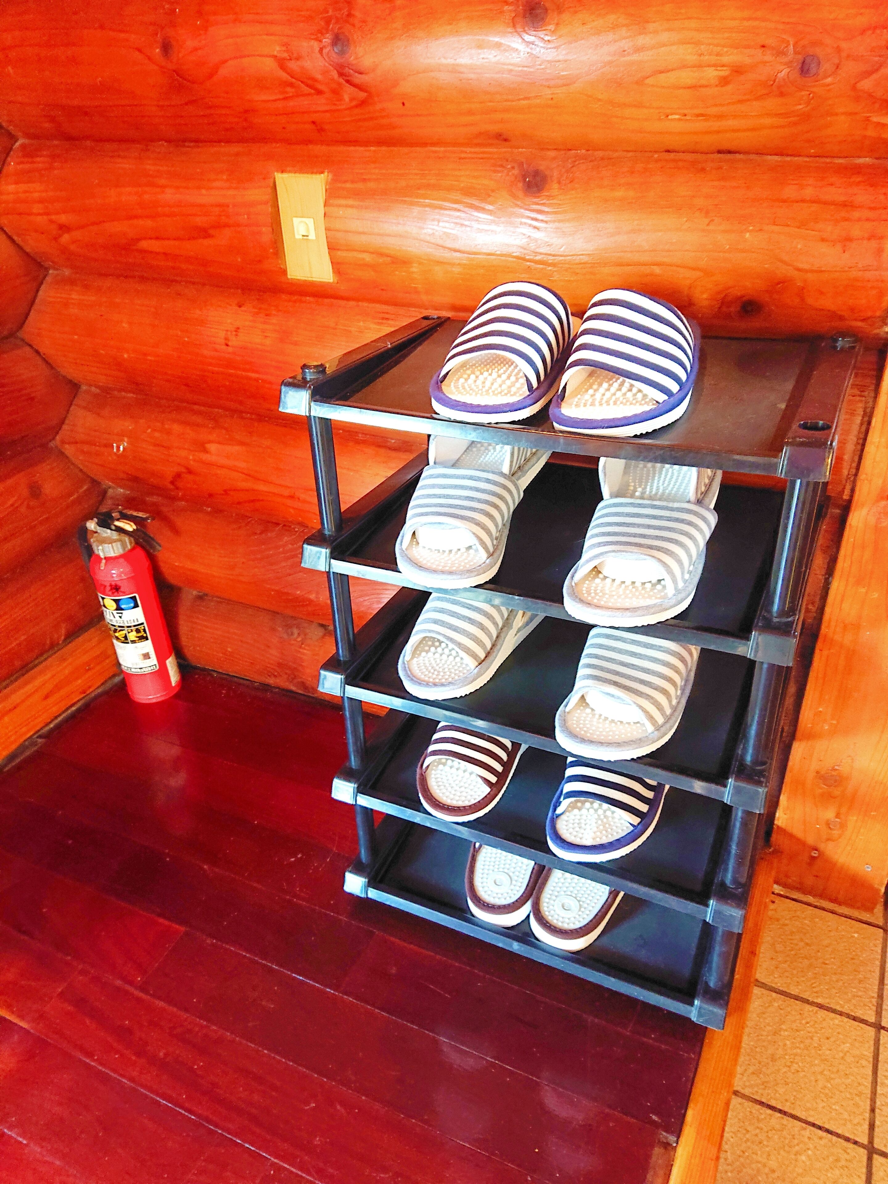 A wooden interior with a metal rack holding multiple pairs of striped slippers. A fire extinguisher is visible on the floor to the left.