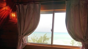 Habitación tipo cabaña con dos camas, una ventana con cortinas, un bote de basura pequeño y una pared de madera.