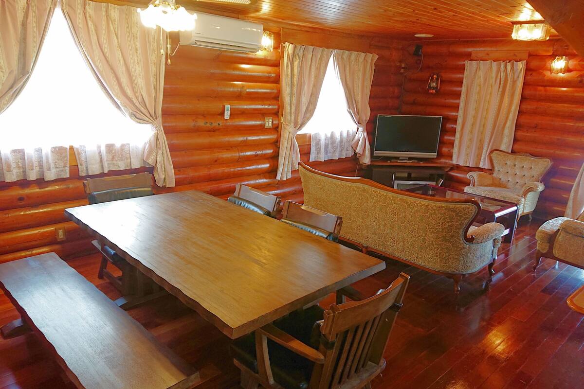 Ein rustikales Blockhaus-Interieur mit einem Holzespeisesaal, gepolsterten Stühlen, einem Fernseher und einem Kamin.