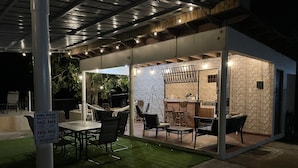 Un espace extérieur aménagé pour les repas, avec des sièges disposés autour de la piscine, un bar et un panneau indiquant les règles à respecter au bord de la piscine.