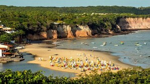 A beach with a sandy shore, boats, and a cliffside with vegetation.