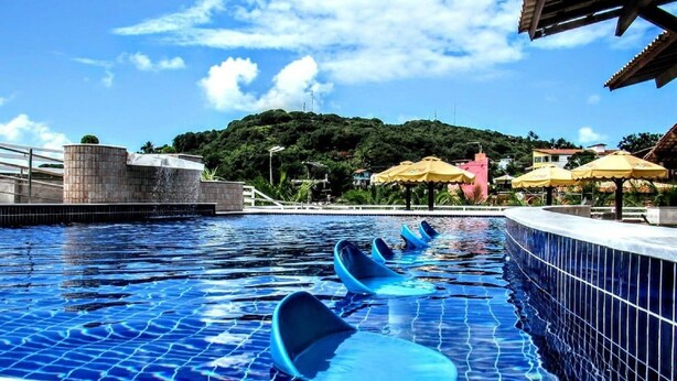 A swimming pool with blue water, a tiled edge, and a few lounge chairs.