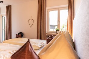 Una camera d'albergo con un letto, una decorazione a forma di cuore sulla parete, una finestra vista verde e una pianta in vaso sul davanzale.