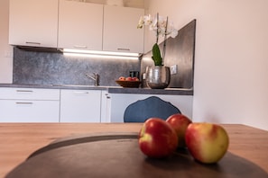 A kitchen with white cabinets, a stainless steel sink, a bowl of fruit, and a vase with flowers.