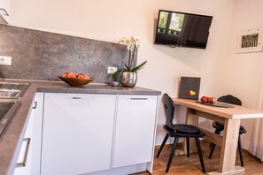 A modern kitchen with a built-in oven, a wooden bowl of fruit, a potted plant, and a television mounted on the wall.