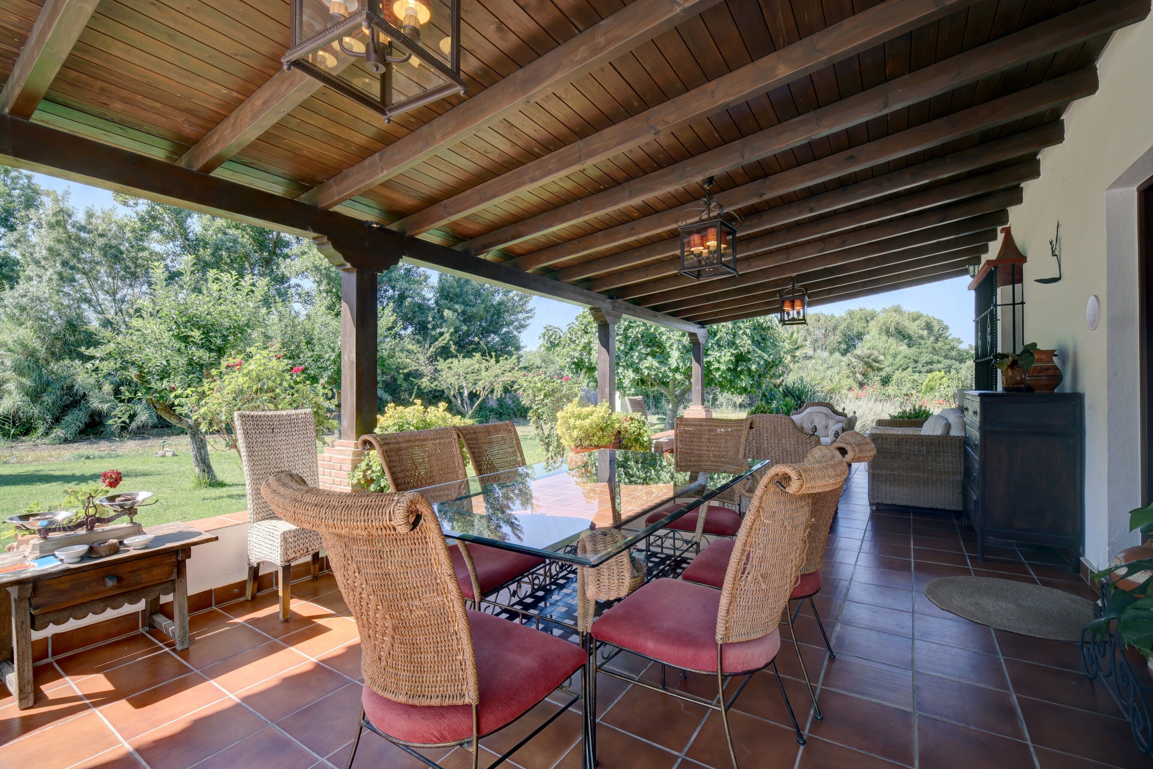 Une terrasse extérieure avec une table à plateau de verre, des chaises en osier et une vue sur le jardin.