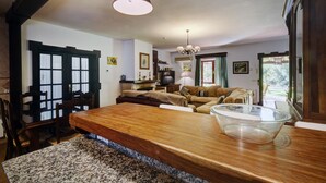 A dining area with a wooden table, chairs, a chandelier, and a large window with curtains.