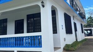 Ein zweistöckiges Gebäude mit weißer Fassade und blauen Akzenten, inklusive eines Balkons mit Balustrade und einer schwarzen Laterne.