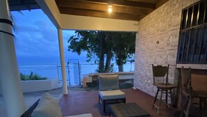 Eine Terrasse im Freien mit Korbmöbeln, einer Steinmauer und Blick aufs Meer.