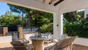 An outdoor patio with wicker furniture, a round table, and a view of the surrounding greenery.