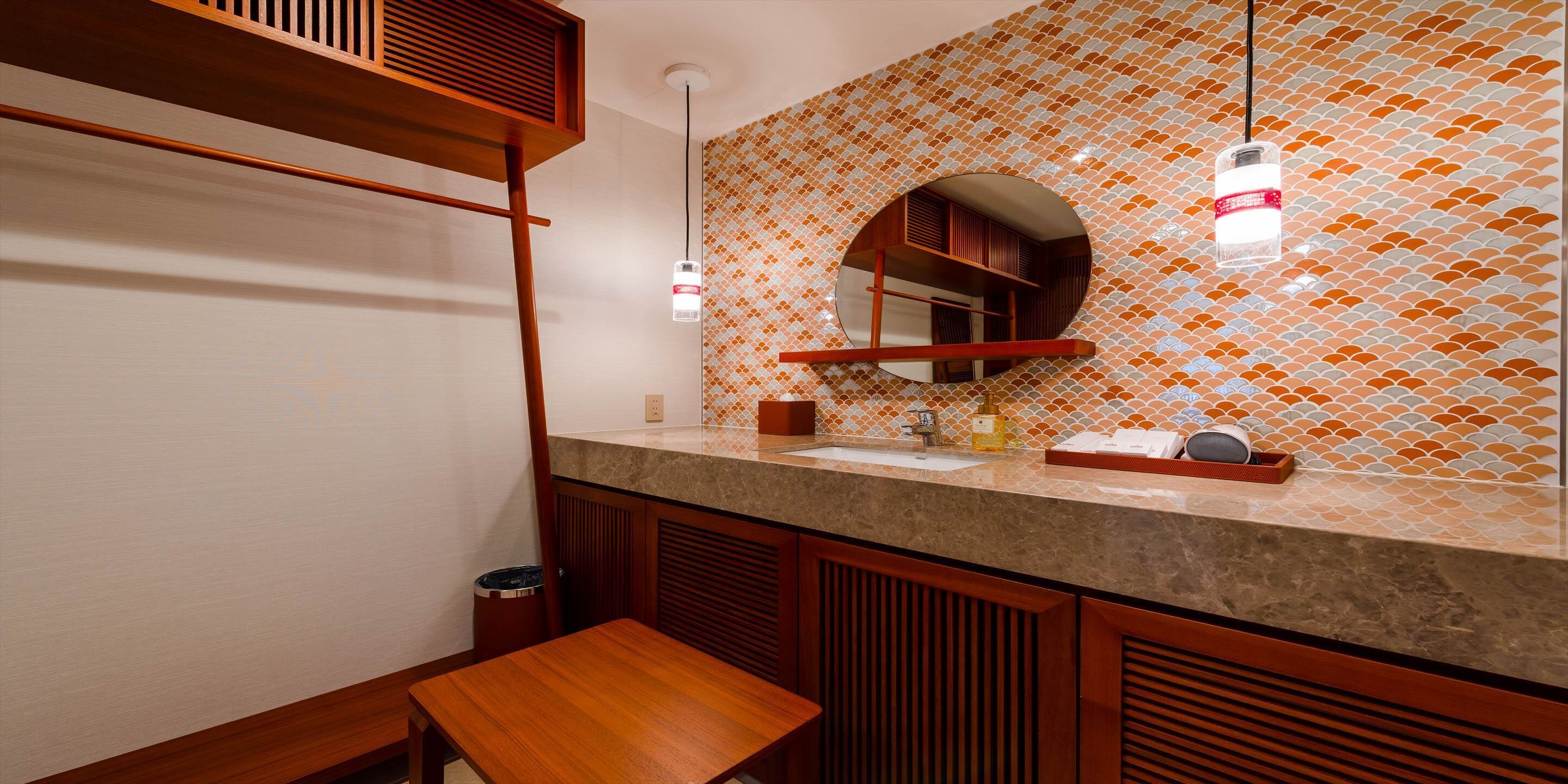 Casa de banho com toucador de madeira, lavatório e espelho com painel de azulejos.
