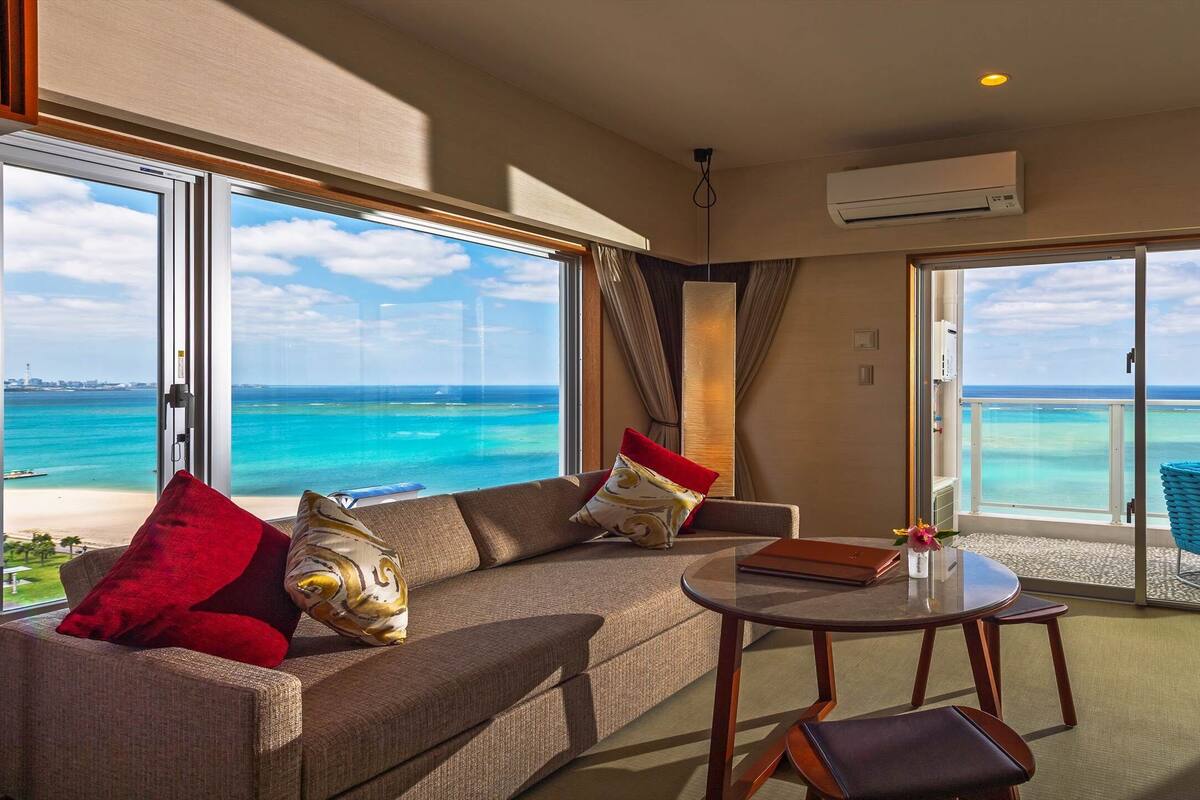 A spacious room with a large sofa, a round table, and a view of the ocean through large sliding glass doors.