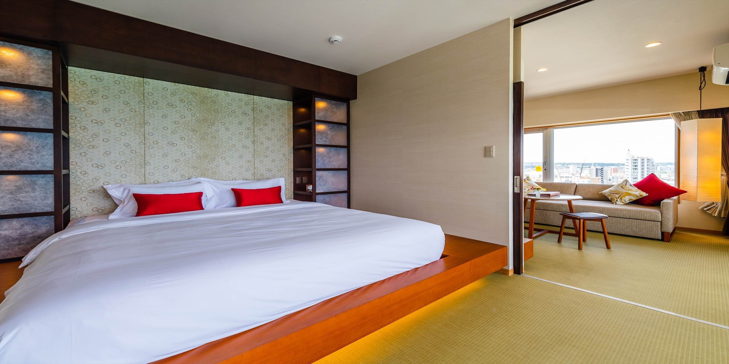 A modern hotel room with a large bed, a sofa, and a view of the city.