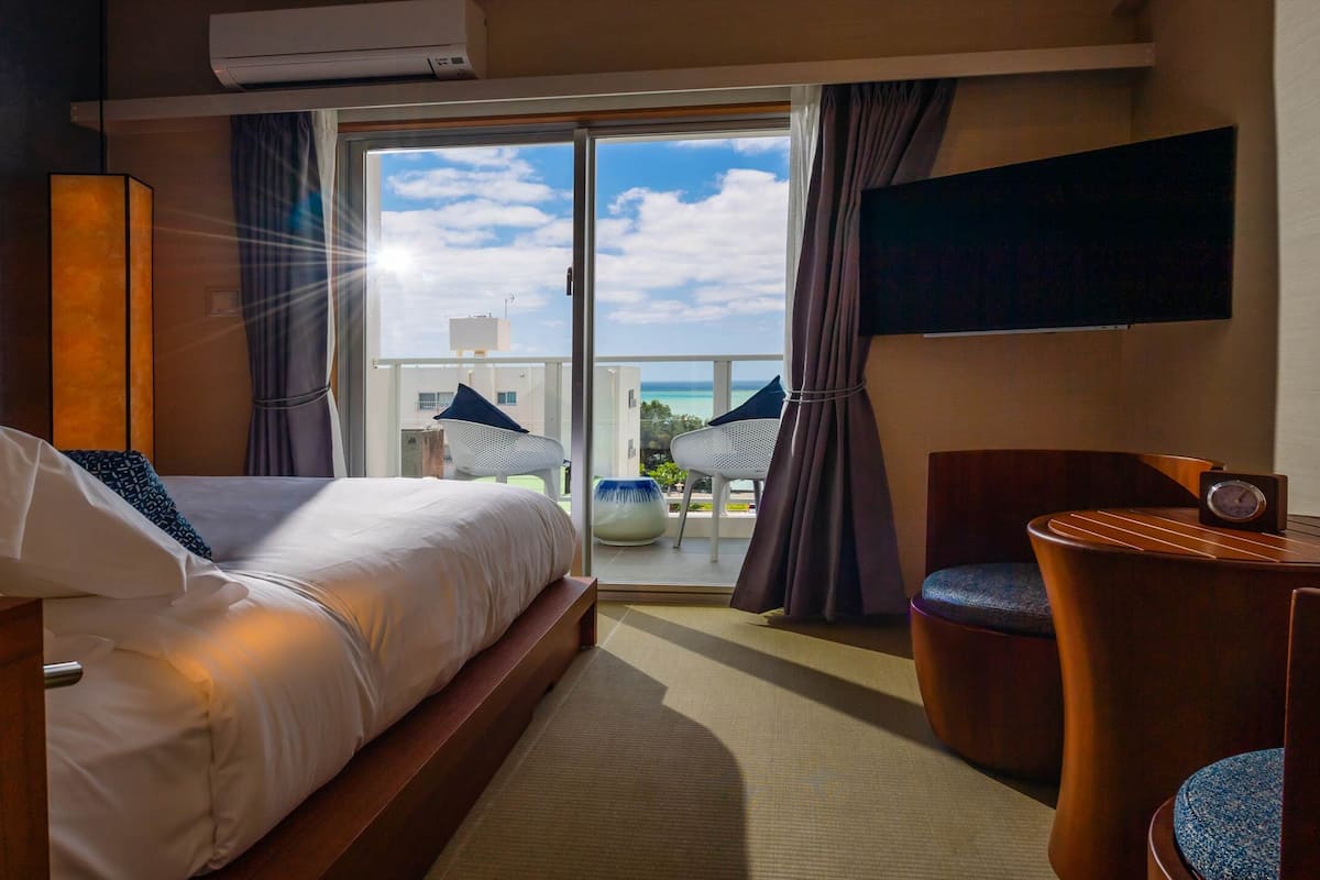 A hotel room with a bed, a small table, a chair, and a TV on the wall.