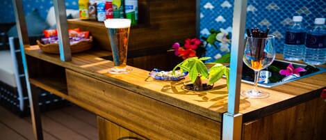A bar area with a tall glass of beer, a small plant, and a glass with a drink. There are bottles and snacks on the counter.