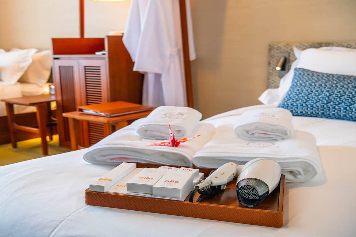 A hotel room with a neatly made bed, a bedside table with a lamp, and a tray with toiletries.