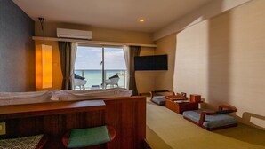 Une chambre d’hôtel avec un lit, un bureau, deux chaises, une télévision et une vue sur la mer.