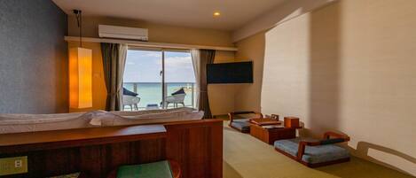 A hotel room with a bed, a desk, two chairs, a TV, and a view of the sea.
