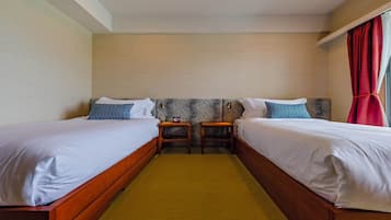 Camera d'albergo con due letti singoli, un tavolino e una sedia.