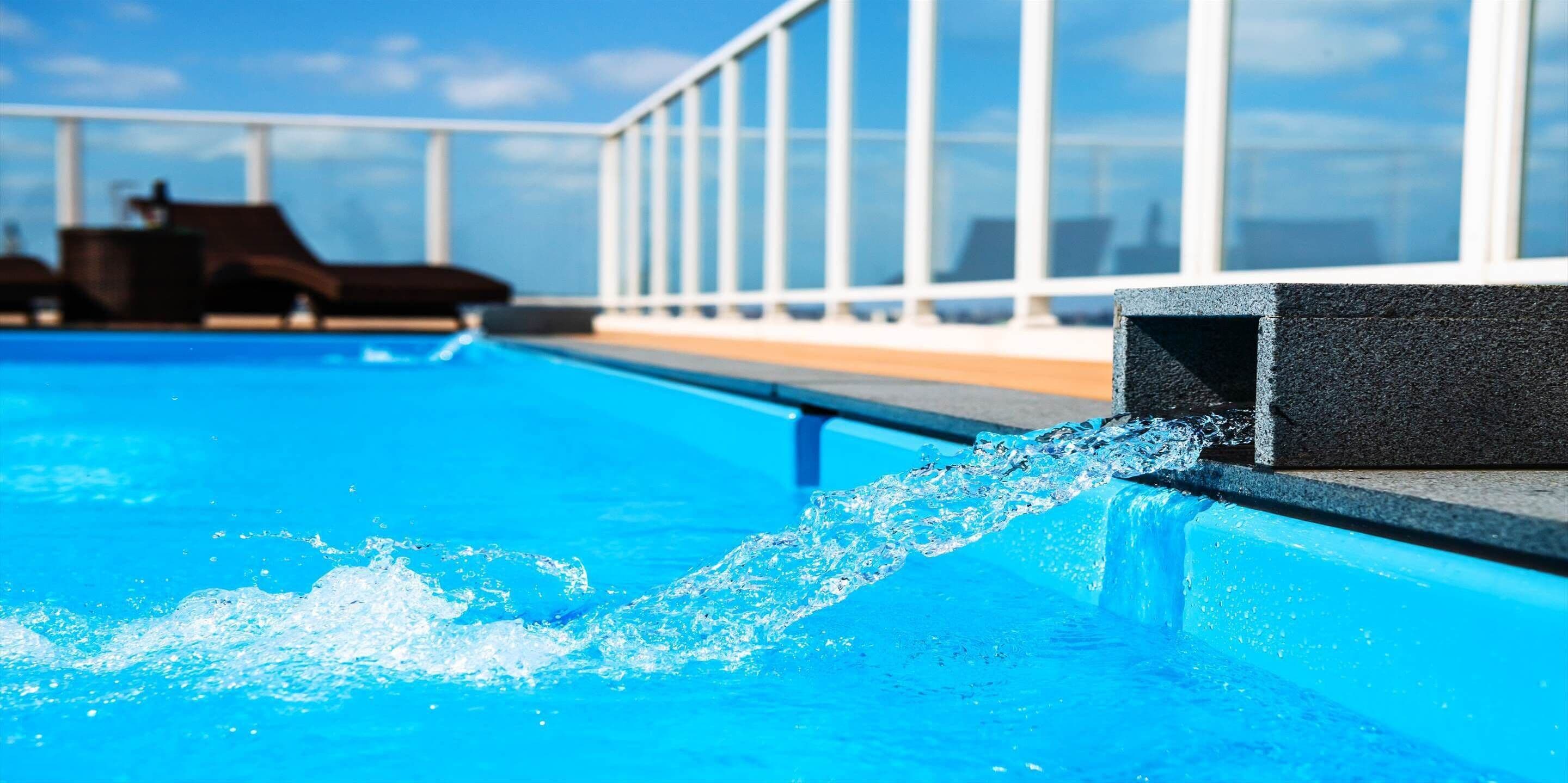 Una piscina con agua azul cristalina, borde negro y vista al océano y un edificio con grandes ventanales al fondo.