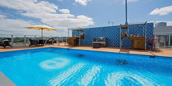 A rooftop pool with lounge chairs, a bar area, and a view of the cityscape. - oile by Zayra Resorts (Chatan)