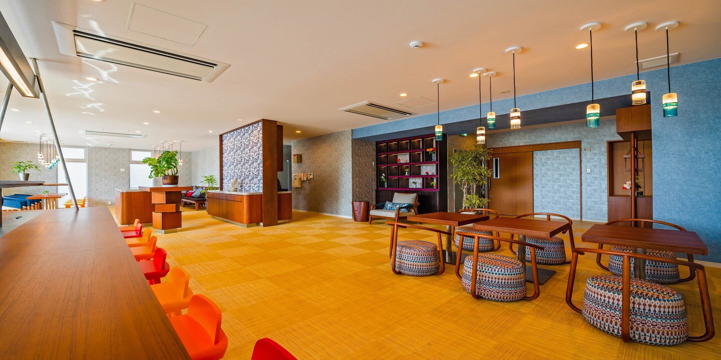 En moderne hotellobby med en lang receptionsdisk, et siddeområde med borde og stole, samt en reol.