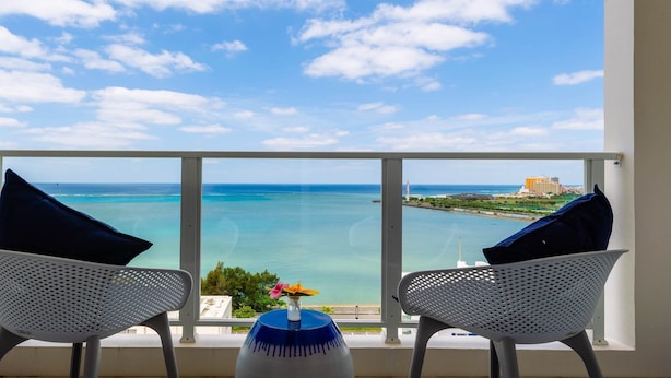 Un balcon avec deux chaises donnant sur la mer, un vase rempli de fleurs et un ciel dégagé.