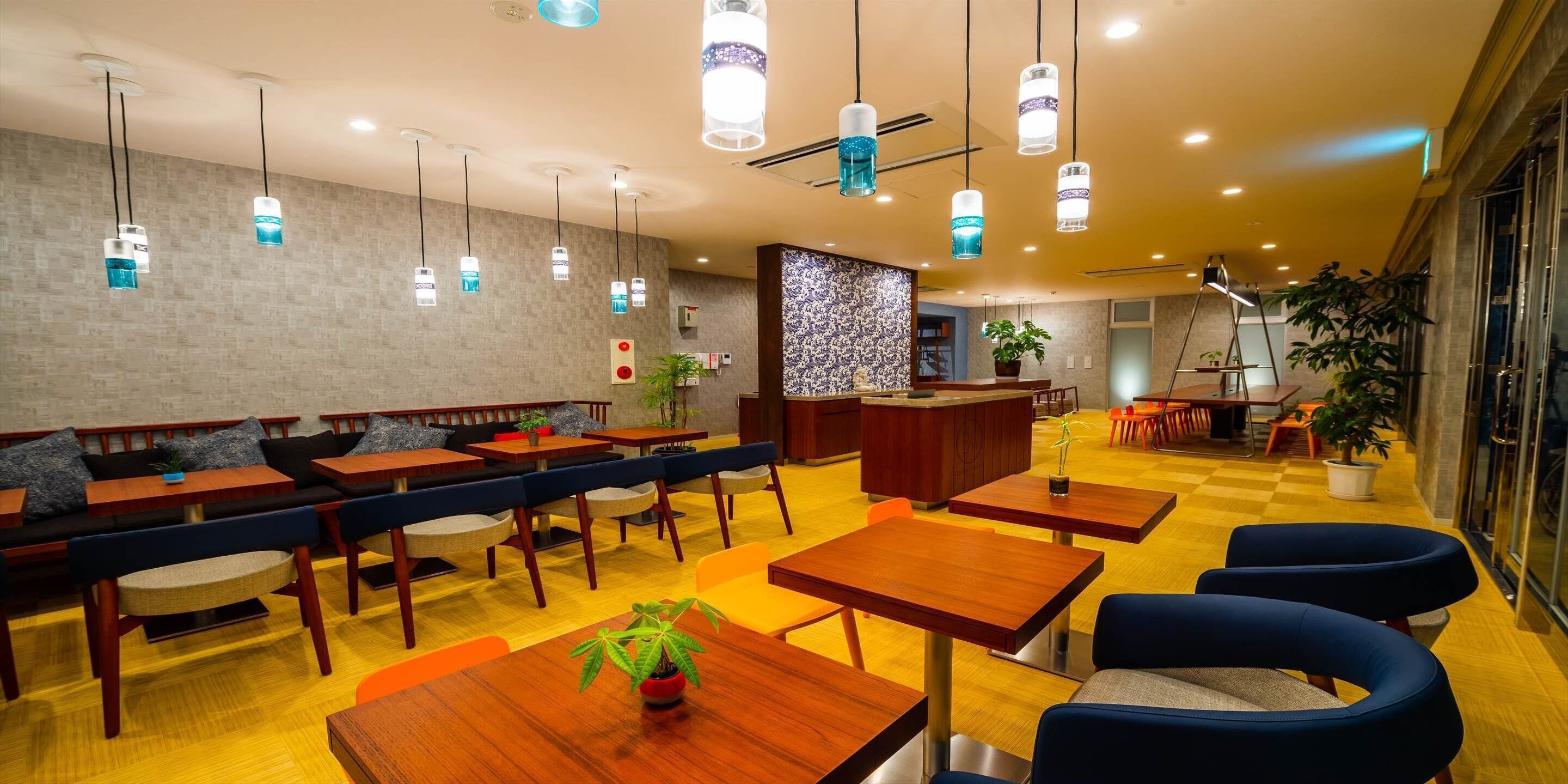 Een modern restaurant met houten tafels, blauw gestoffeerde zitplaatsen, een bar in het midden en hangende hanglampen.