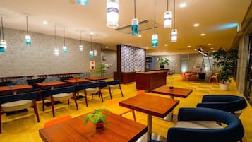 Un restaurant modern amb taules de fusta i seients blaus amb coixins, una zona de bar central i llums penjants.