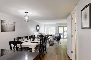 A dining area with a white table and chairs, a hanging light fixture, and a view of the beach through the window. - Guest Favorite Courtside Villa walk to Beach | 2 Pools, Tennis, Balcony | Coligny Area Fun! (Hilton Head Island)