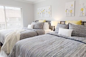 A bedroom with two beds, a bedside table with a lamp, and artwork on the wall. - Guest Favorite Courtside Villa walk to Beach | 2 Pools, Tennis, Balcony | Coligny Area Fun! (Hilton Head Island)
