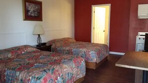 Una habitación con dos camas, una mesa, una lámpara y una puerta que da a otra estancia.