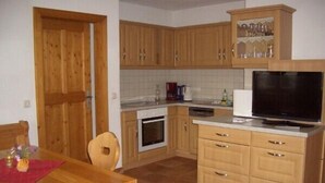 A compact kitchen with wooden cabinets, a built-in oven, a dishwasher, and a television.