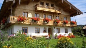 A traditional wooden house with a balcony, surrounded by a well-maintained garden with various flowers.